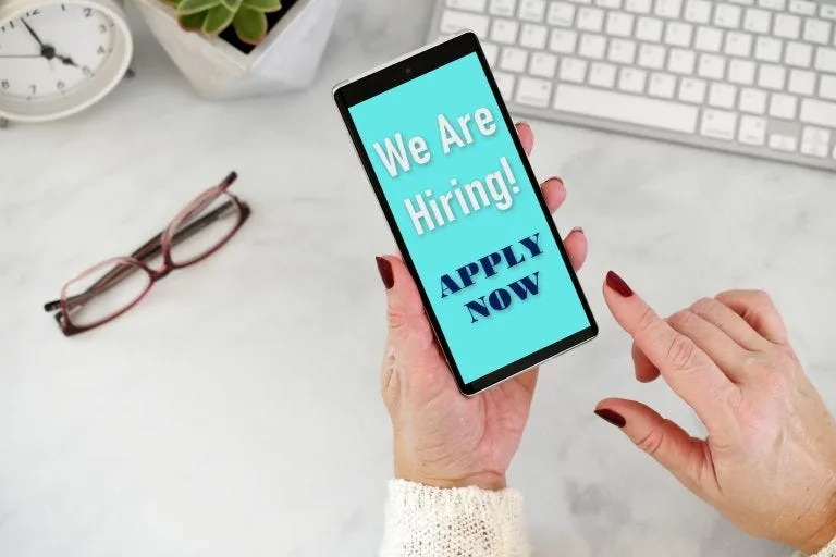 Online Job Search - We are Hiring Apply Now on phone screen with desk in background All items/Photos