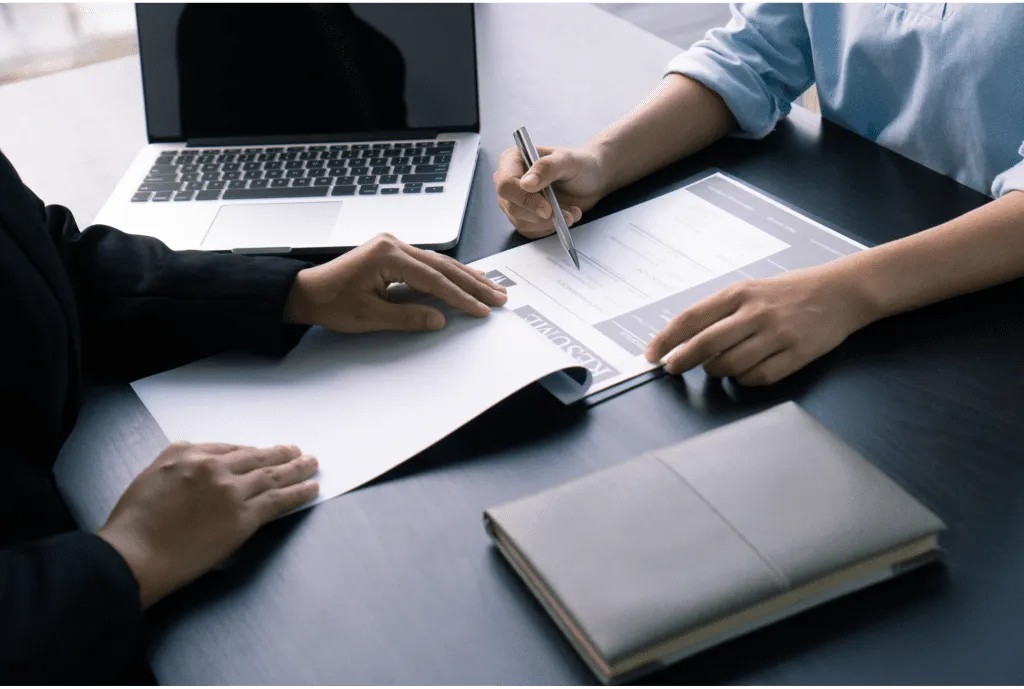 Two individuals at a job interview, with focus on hands and a resume on the table, indicating a professional evaluation or discussion