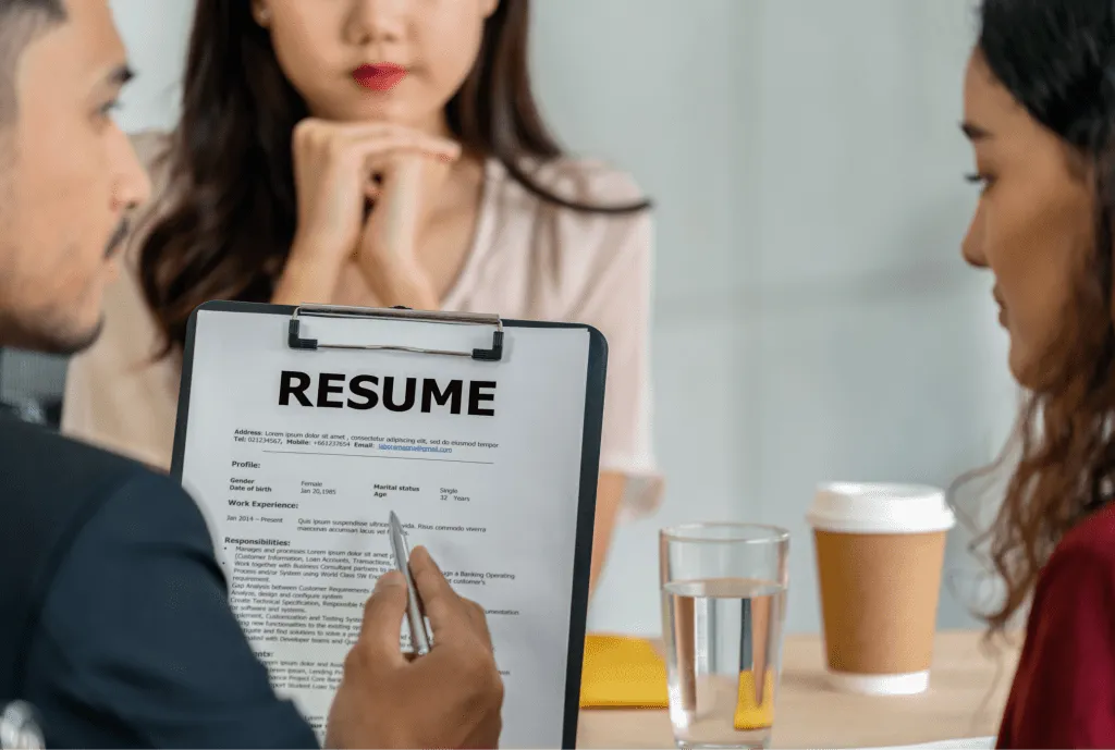 Interviewer holding a resume with a job candidate and beverages on the table, depicting a professional job interview scene.