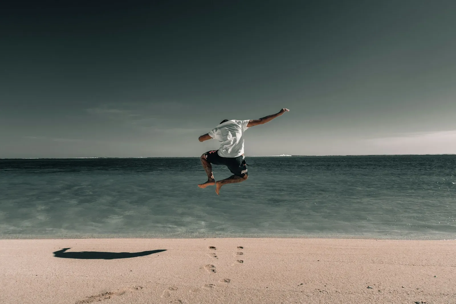 Young man jumping on the beach, enjoying the ocean view during sunset or sunrise.