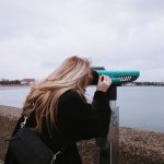 woman in black jacket holding green and white plastic cup near body of water during daytime